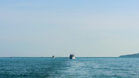 a fishing boat moves steadily across calm waters in phuket, thailand, under clear skies with a distant shoreline