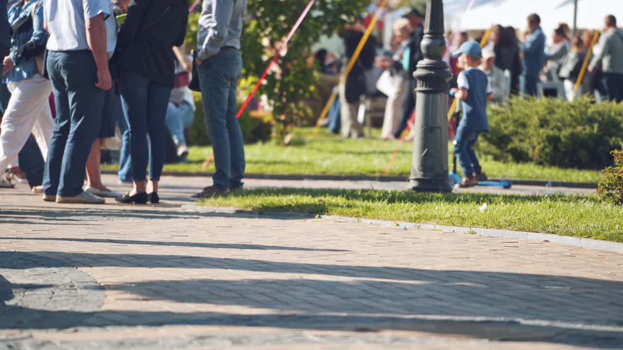 Unrecognizable people walking in the city. Sidewalk and legs of crowds of people moving along slowly in summer. People resting in the city park.