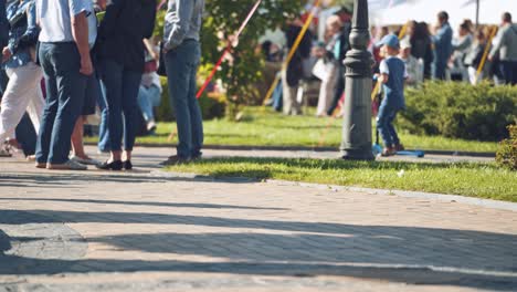 unrecognizable people walking in the city. sidewalk and legs of crowds of people moving along slowly in summer. people resting in the city park.