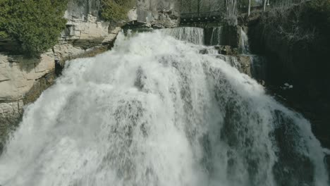 The-rushing-owen-sound-waterfall-surrounded-by-rugged-cliffs-in-ontario,-canada,-in-daylight,-aerial-view