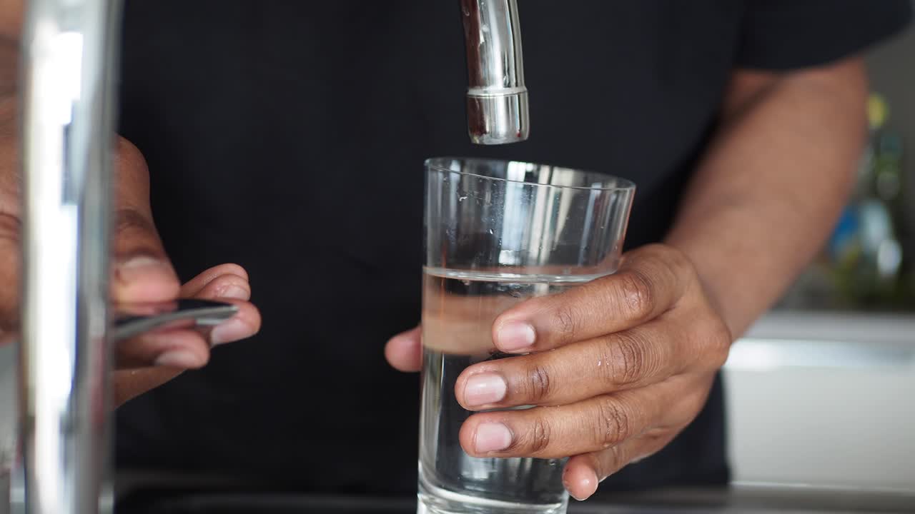 persona llenando un vaso con agua de un grifo de la cocina
