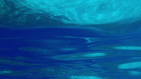 real underwater view of turquoise sea water surface undulating and rays of light reflecting