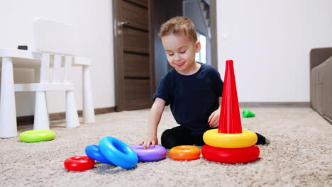 smiling caucasian baby assembles a toy pyramid. cheerful kid puts the rings on the basis.