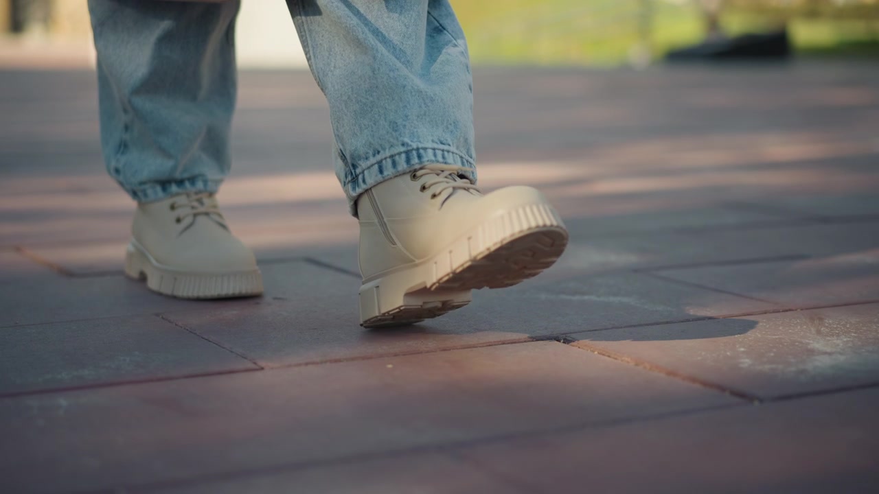 Close up of person feet in light blue jeans and beige lace up shoes walking on red brick pavement. focus remains solely on lower legs footwear details like laces texture are visible