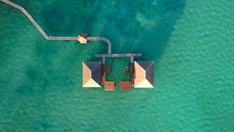 top down view of a water bungalow with wooden bridges surrounded by beautiful turquoise water, drone flying up at leebong island in belitung indonesia