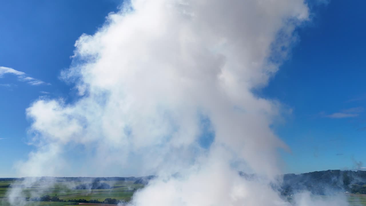 Aerial footage of smoke rising from a stack against a clear blue sky over agricultural fields