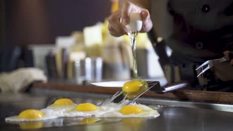 chef cracks egg above steel spatula to make them slide onto hot plate, slowmo hd