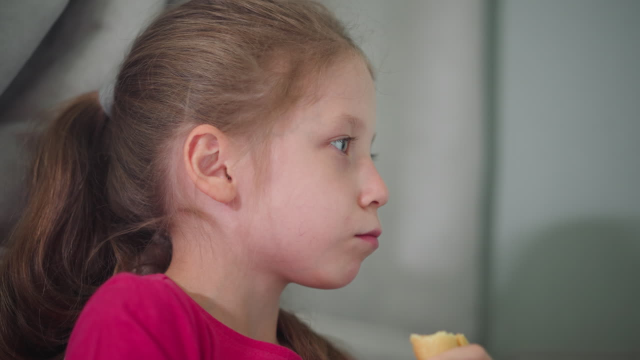 Close up of little girl in red top savoring her cake with a happy expression indoors showing joy of childhood indulgence as she enjoys snack time in a calm and cozy home environment