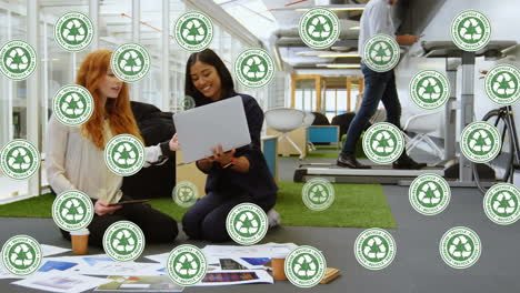 animation of recycling icons over happy diverse female coworkers in office