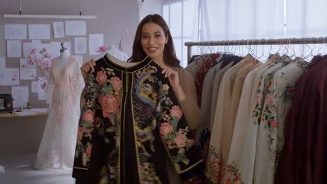 woman fashion designer showcasing embroidered garments in her studio
