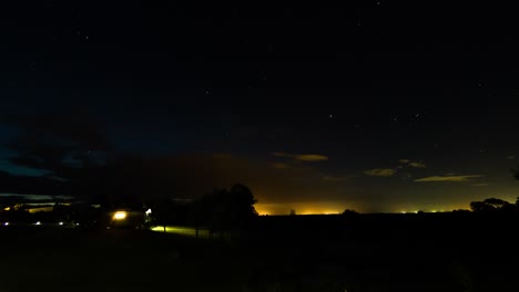 Tranquil-Hunter-Valley-nightlapse-with-lights-glowing-on-the-horizon,-low-whipsy-clouds-and-stars
