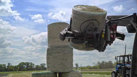 Agricultural-machinery-transporting-straw-rolls-on-farming-field.-Haystacks