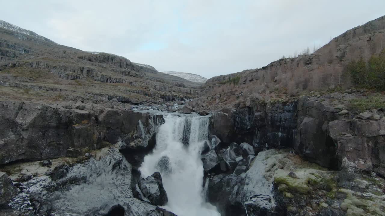 drone volando sobre una hermosa y amplia cascada, hacia un río lleno de rocas en islandia