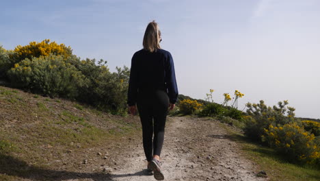 young woman walks along a path overflowing with vegetation on the sides