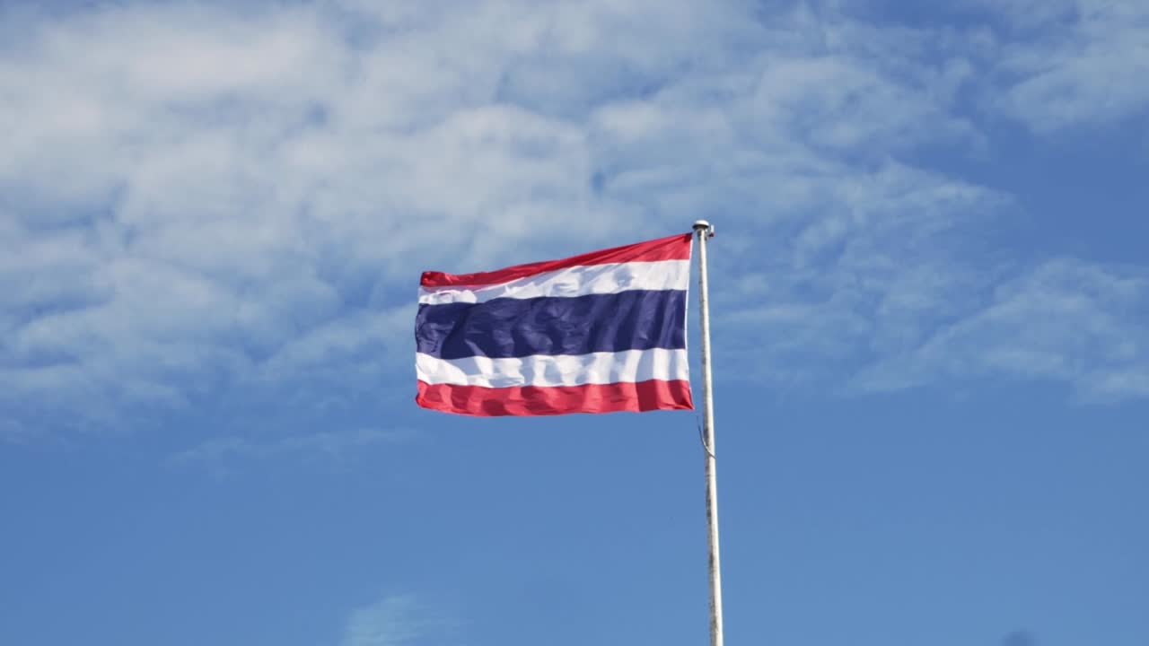 파란 하늘 과  ⁇  구름 을 배경 으로 한 기둥 에 태국 국기 를 흔들고 있다