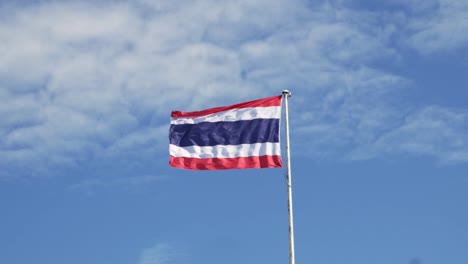 Waving-the-Kingdom-of-Thailand-flag-on-a-pole-with-blue-sky-and-white-clouds-in-the-background