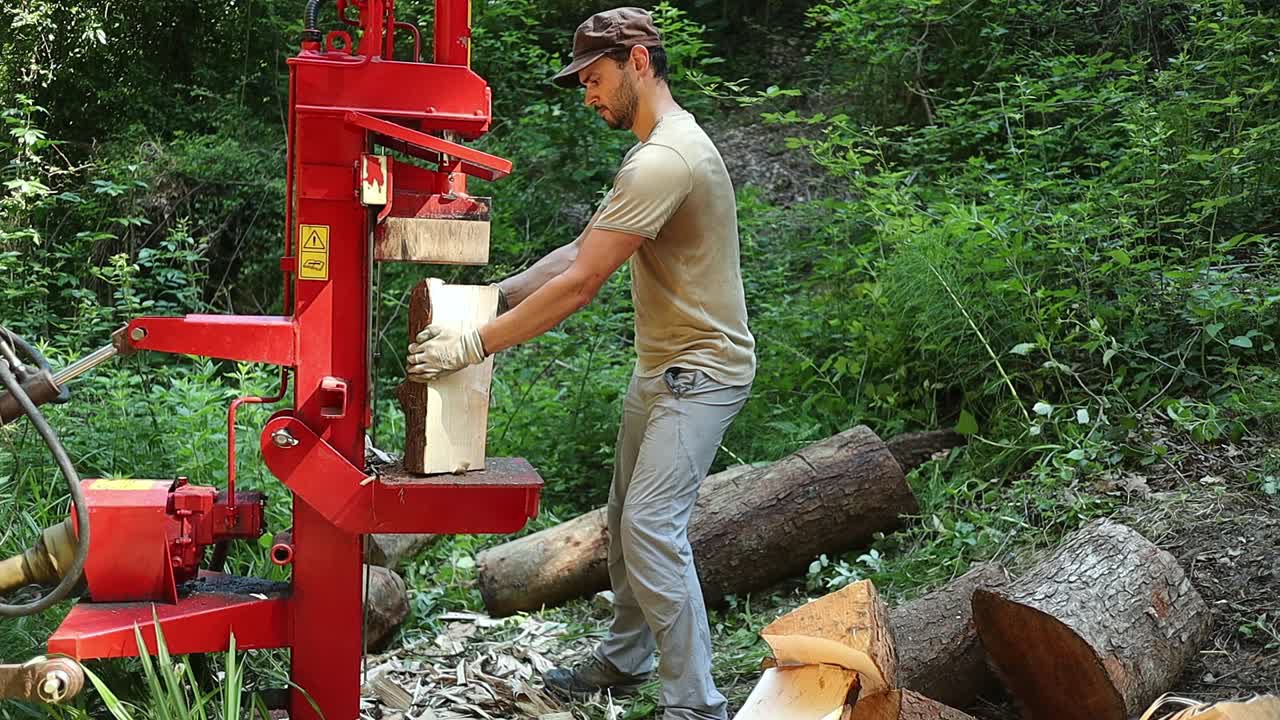 A man surrounded by small logs that he is cutting up with a hydraulic wood splitter