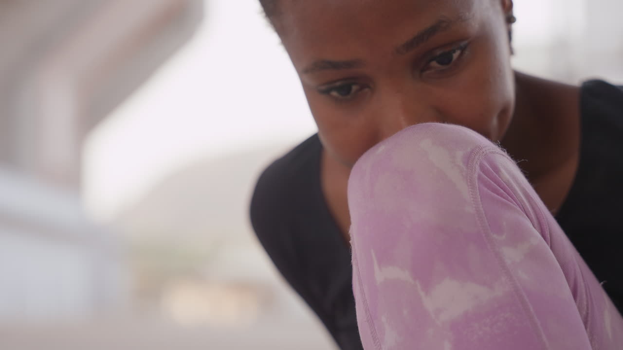 black girl under bridge looking pensive, wearing purple leggings and braided hair, pausing between rehearsal and commute, shifting roles from student to dancer to commuter, concrete backdrop with soft