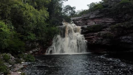 Aerial-drone-dolly-out-shot-of-the-stunning-Devil's-Pit-waterfall-surrounded-by-rocks-and-jungle-foliage-in-the-beautiful-Chapada-Diamantina-National-Park-in-Northeastern-Brazil-on-an-overcast-day