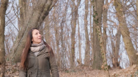 Brunette-Woman-Wearing-Winter-Jacket-Walking-In-Forest-And-Looking-Around-On-A-Sunny-Day