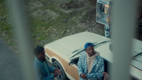 african american man talking to friends by car parked on gritty urban street