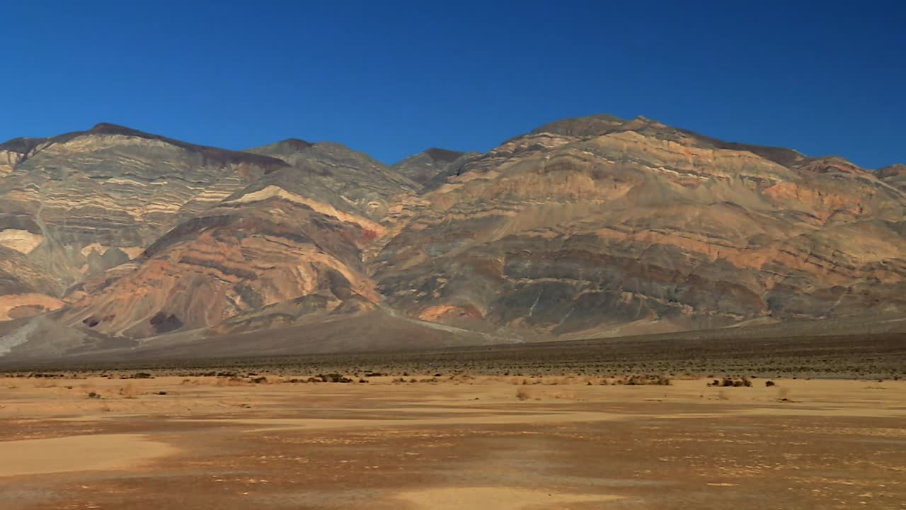Striated multicolored rock formations and dry desert plain at the base of rugged mountains in Death Valley National Park, California, USA