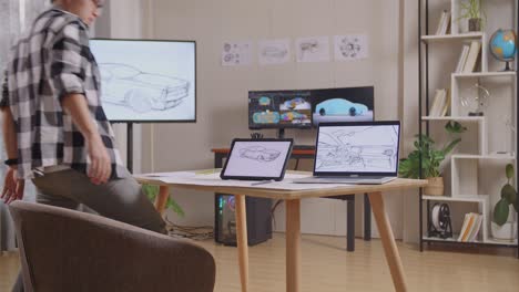 vista lateral de un hombre asiático caminando para sentarse y dibujar un nuevo concepto de diseño de automóvil en una tableta en el estudio con televisión y computadoras muestra modelo de automóvil eléctrico 3d