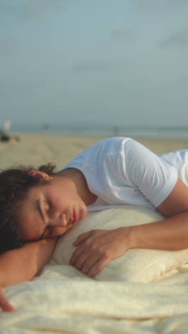 indian woman in white t-shirt rests on cushion atop blanket, eyes closed under morning sun
