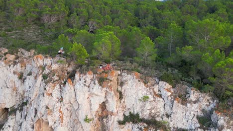 Wanderer-Ruhen-Sich-Auf-Einer-Felsklippe-Zwischen-Bäumen-Aus-Und-Haben-Bei-Sonnenuntergang-Auf-Ibiza-Blick-Auf-Die-Grüne-Landschaft