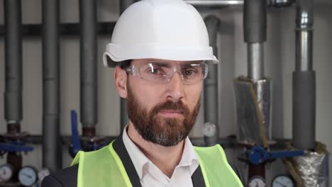portrait of confident professional contractor in hard hat or safety wear or engineer worker wearing uniform, glasses in boiler room. male qualified specialist standing near water pipes.