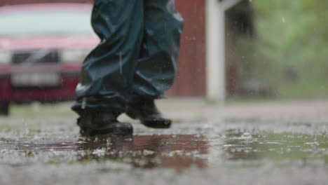 slow motion, a child in wet weather gear walks through the heavy rain