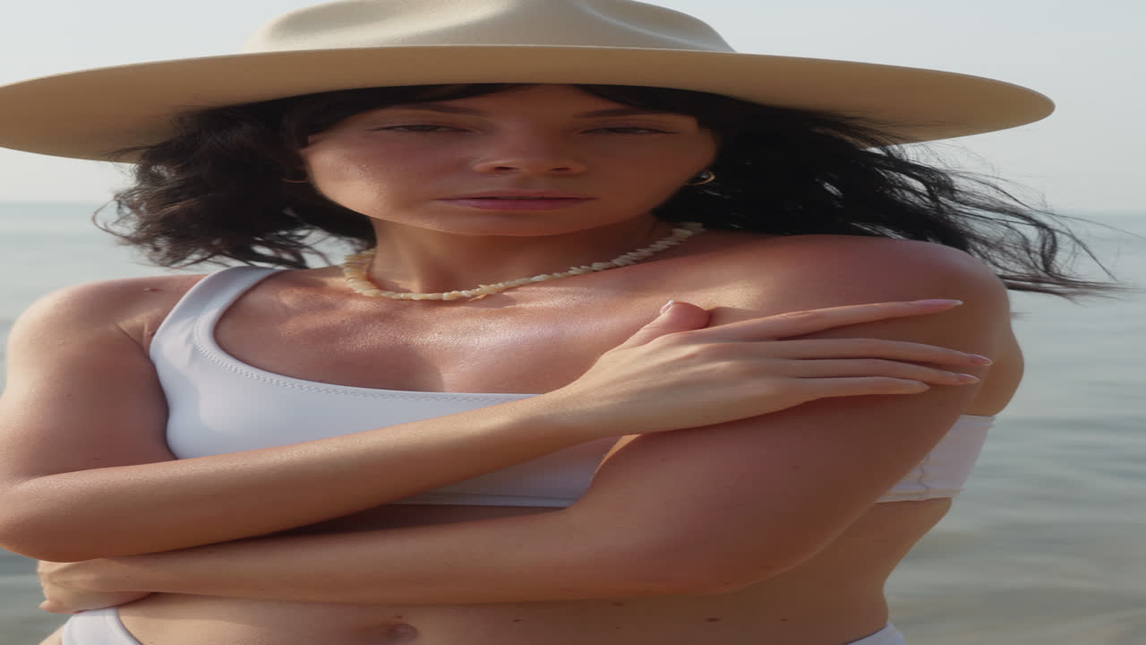 Giovane donna con cappello e bikini bianco in posa vicino all'acqua