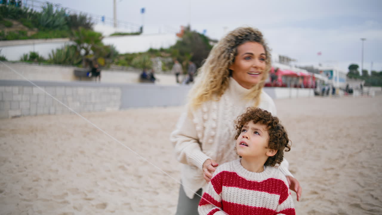 Famiglia che trascorre del tempo insieme su una spiaggia autunnale. Un bambino riccio che lancia un aquilone.
