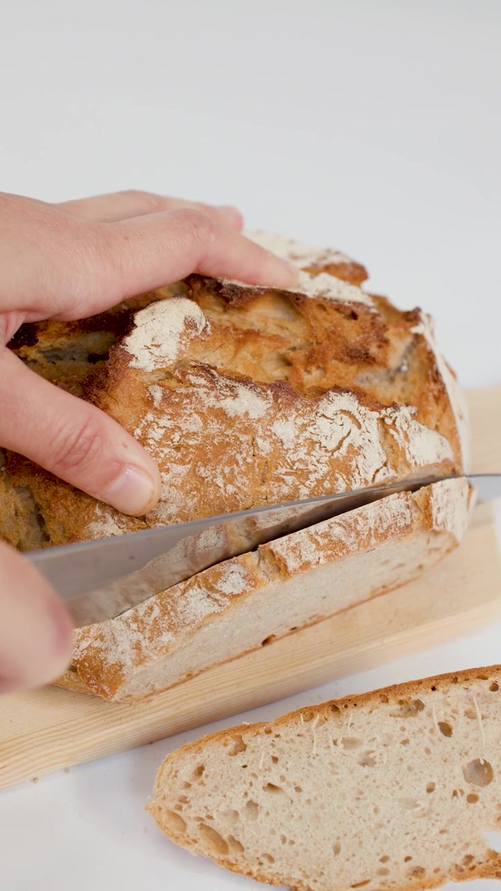 Hand Slicing Fresh Crusty Sourdough Bread on Wooden Board