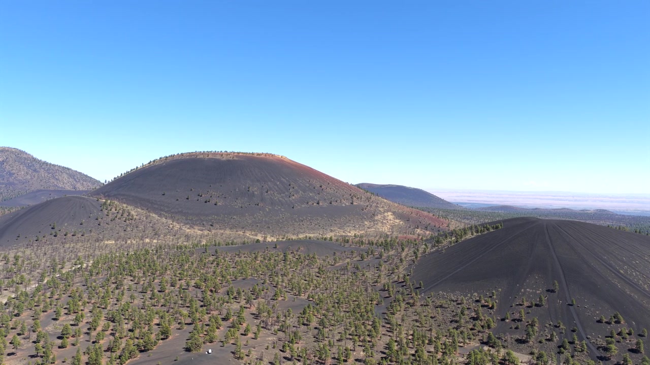 Filmato drone 4K fluido che riprende un cono di scorie vulcaniche tra un'antica foresta di pini ponderosa in Arizona. La vista aerea panoramica evidenzia la vegetazione unica di alta quota e la geologia aspra del sud-ovest.