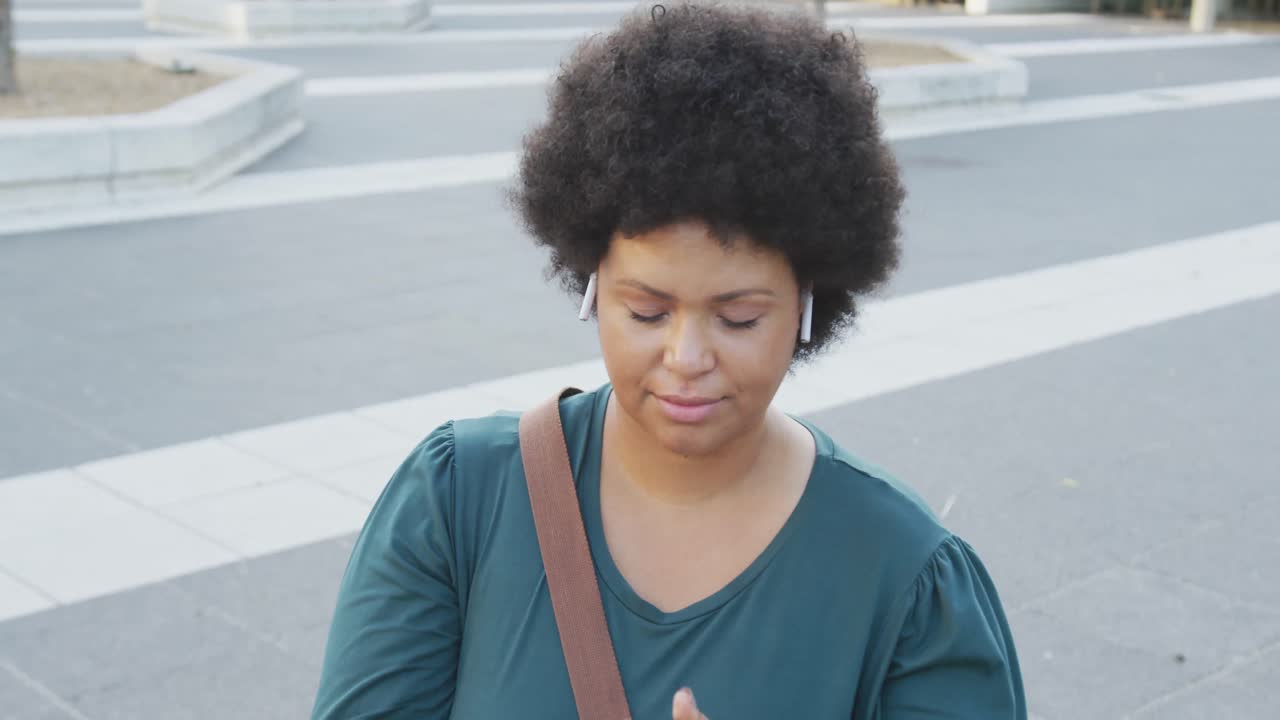 Donna birazziale formosa e felice che usa lo smartphone e indossa gli auricolari in città.
