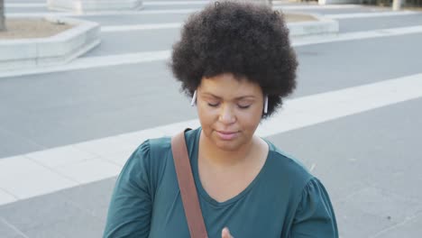 happy plus size biracial woman using smartphone and wearing earphones in city