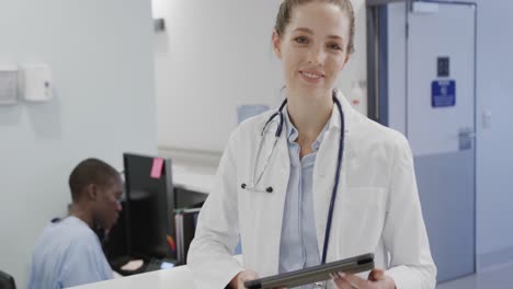 porträt einer kaukasischen ärztin mit einem lächelnden tablet an der empfangsstelle des krankenhauses, in zeitlupe