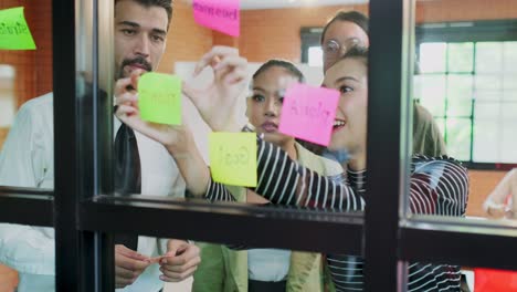 diversity of young business people group have discussion meeting in office. man, woman have communication brainstorming and put sticky note it on wall together. corporate teamwork of modern colleague.