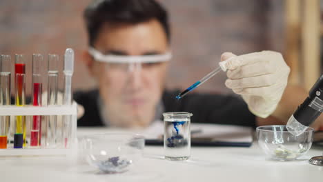 student in gloves drops blue liquid into clear water in lab