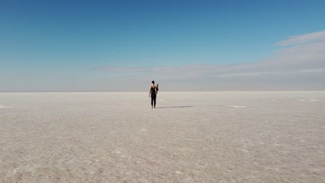 beautiful young woman walking with a yoga mat in the middle of a salt flat