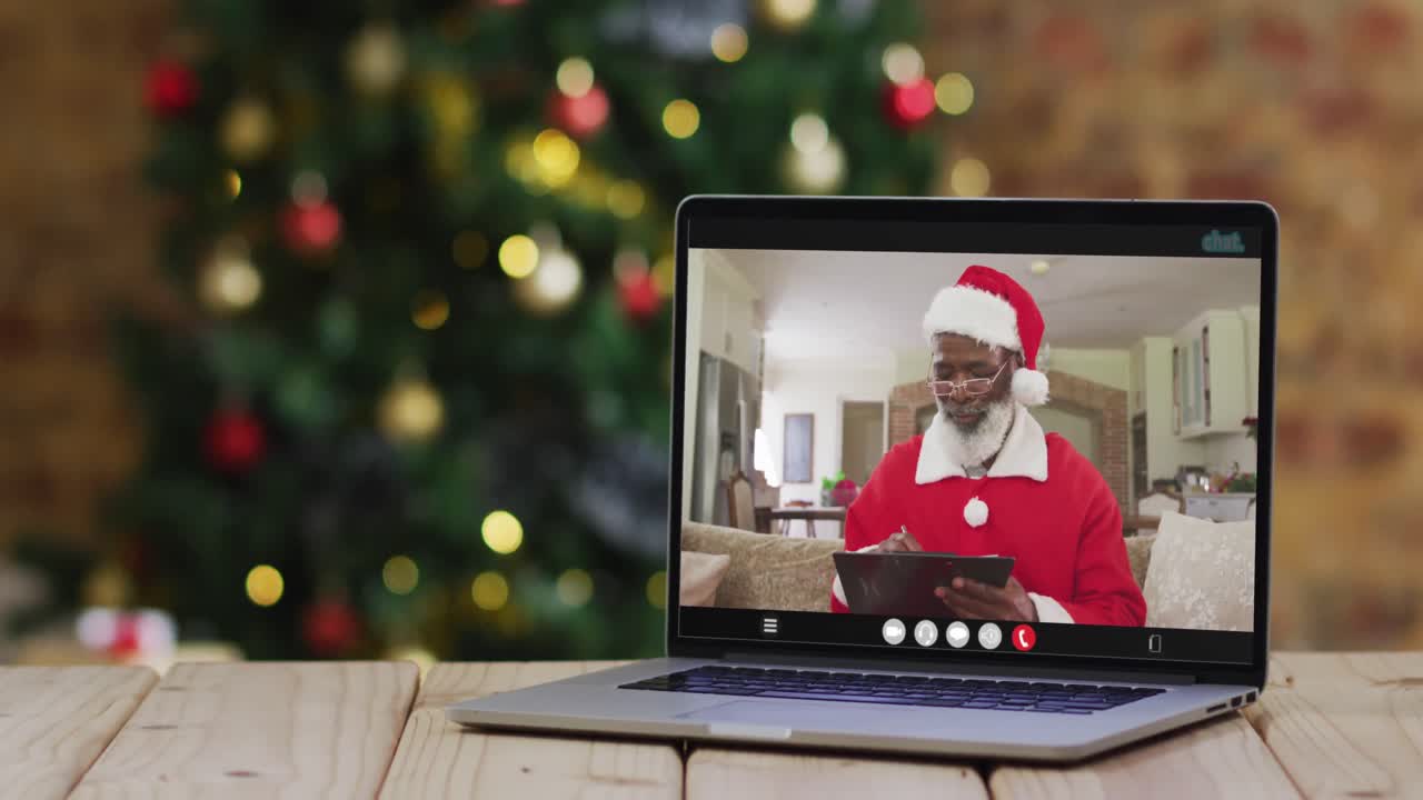 hombre afroamericano senior en disfraz de santa en videollamada en computadora portátil, con árbol de navidad
