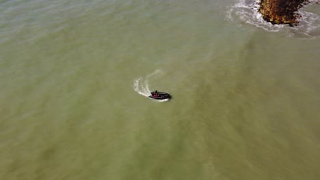 Toma-Aérea-De-Un-Bote-Inflable-Negro-Que-Navega-De-Regreso-A-La-Costa-De-Mar-Del-Plata-Durante-El-Verano,-Argentina