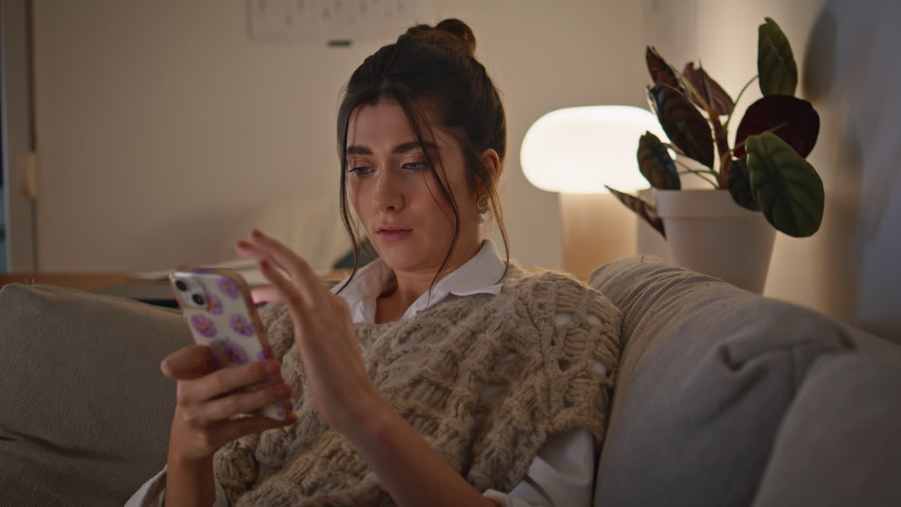 mujer relajada usando el teléfono móvil descansando en el sofá en closeup nocturno. señora escalofriante