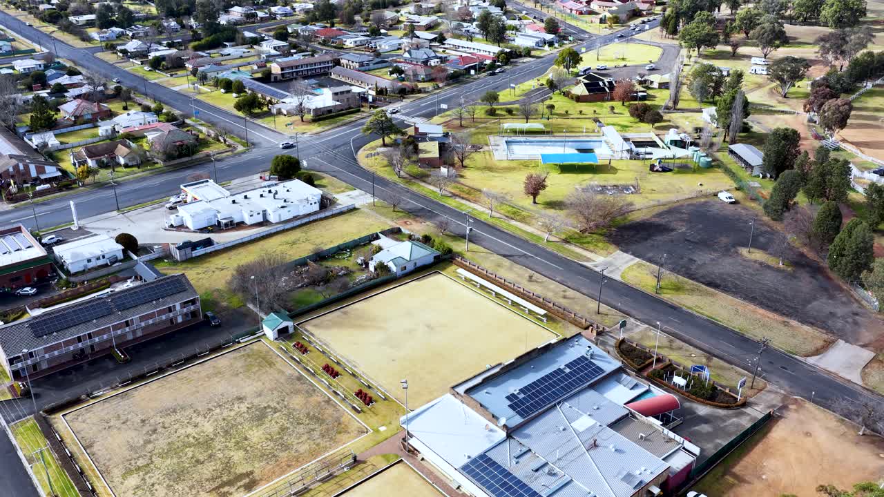 Drone footage glides above residential streets, community buildings, and green spaces in Coonabarabran, NSW, under bright daylight with steady, smooth camera movement