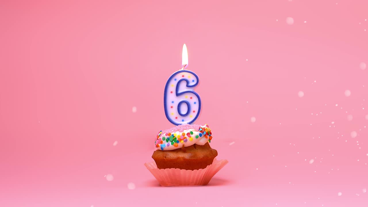 primer plano de una magdalena de celebración de cumpleaños feliz con glaseado, chispas y una llama de vela encendida de 6 años de edad ardiendo y moviéndose sobre un fondo de coral rosa - bucle de boomerang sin fisuras