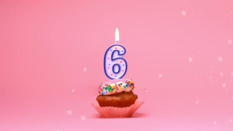 close-up de um cupcake de comemoração de feliz aniversário com glacê, confeitos e uma chama de vela acesa de 6 anos queimando e movendo-se em um fundo de coral rosa - loop de bumerangue sem costura