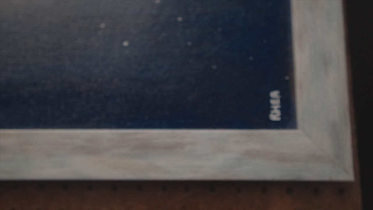 A close-up detail shot of an art piece signed by the artist with the name &amp;quot;Rhea&amp;quot; reveals intricate details, colors, and textures