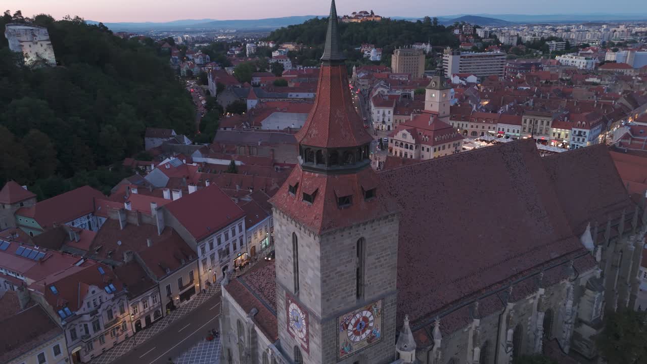 Filmato aereo di un drone che orbita intorno alla torre dell'orologio della Chiesa Nera di notte nella città storica di Brașov, Romania