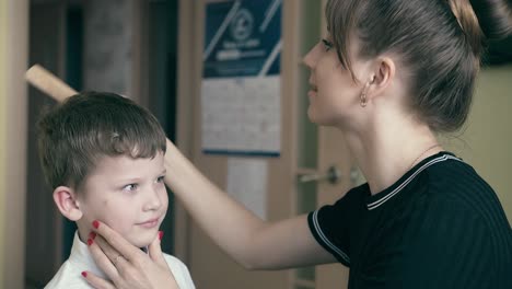 cu joven madre bonita viste a un niño a la escuela peinándolo